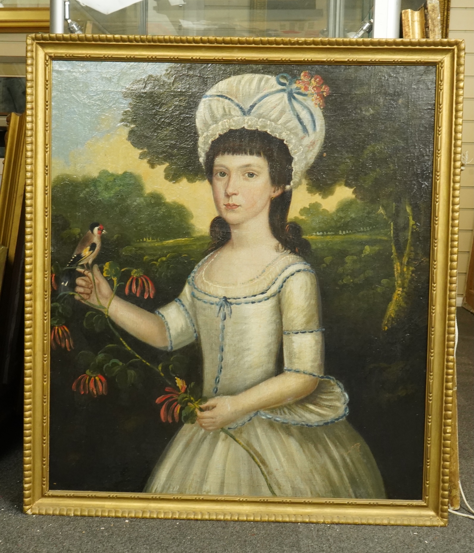 Late 18th century English School, Half length portrait of a young woman, standing in a landscape holding a goldfinch, oil on canvas, 74 x 46cm